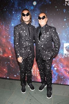 two men in black suits and sunglasses standing next to each other on a red carpet