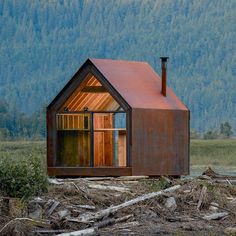 a small cabin sits in the middle of a field with trees and mountains behind it