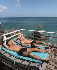 two men lounging on an outdoor deck next to the ocean