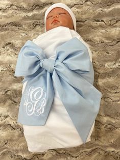 a baby wrapped in a blue and white blanket with a monogrammed bow on it's head