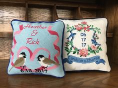 two cross stitch pillows sitting on top of a wooden table