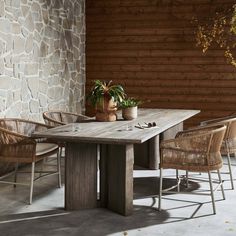 a wooden table with chairs around it in front of a stone wall and potted plant