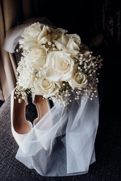 a bouquet of white roses and baby's breath sits on top of a pair of shoes