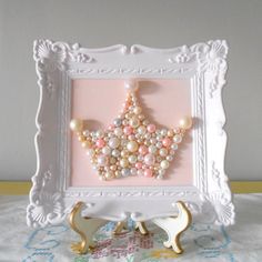 a white frame holding a pink and gray beaded star ornament with pearls