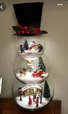 three snow globes with christmas decorations in them on top of a wooden table next to a white wall