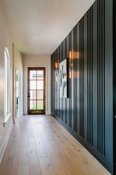 an empty room with wood flooring and black paneling on the wall, next to a large open door