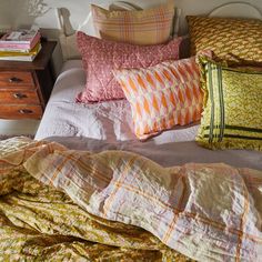 a bed topped with lots of pillows next to a night stand filled with books and flowers