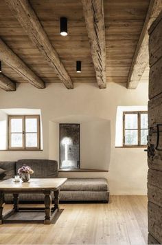 a living room filled with furniture and wooden beams on the ceiling, along with windows