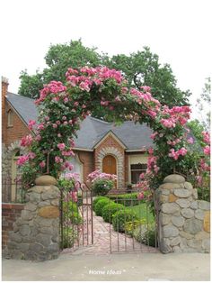 a house with pink flowers growing over it's front gate and stone wall around the entrance