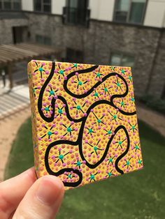 a hand holding up a small square piece of paper with colorful designs on the outside