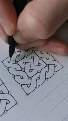 a person is writing on paper with a pen in their hand and an intricate design