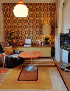 a living room with an orange and yellow wallpaper on the walls, two black chairs, a round wooden table in front of a television