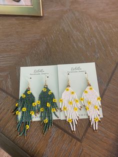 three pairs of beaded earrings sitting on top of a wooden table next to a card