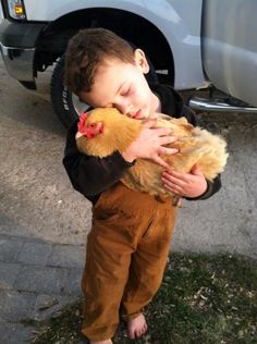 a young boy holding a chicken in his hands while standing next to a parked car