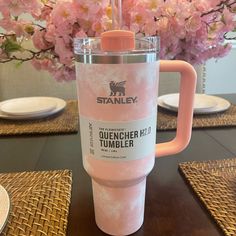 a pink tumbler cup sitting on top of a table next to plates and flowers