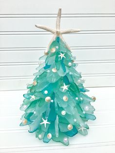 a glass christmas tree with starfish and pearls on the top, sitting in front of a white wall