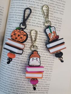 two bookmarks with charms attached to them sitting on top of an open book in the shape of books