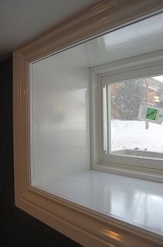 an empty window in the corner of a room with snow on the ground and trees outside