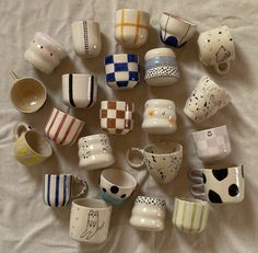 there are many coffee cups on the bed together, all different colors and designs in each cup