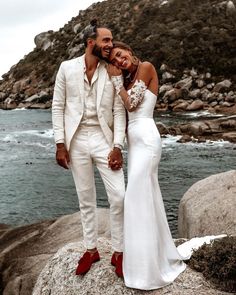 a man and woman are standing on rocks near the water