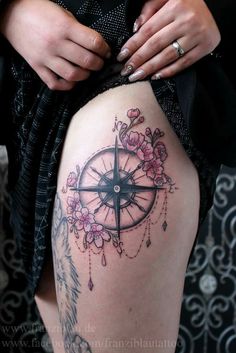 a woman's thigh with a compass and flowers on it