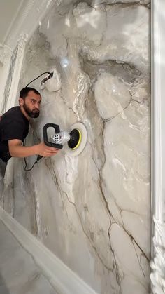 a man using a grinder on a marbled wall in a room with white trim