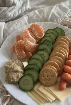 a white plate topped with crackers, cucumbers and carrots next to orange slices