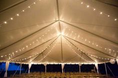 the inside of a large tent with rows of chairs and lights strung from it's ceiling