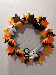 a wreath made out of felt and fake pumpkins with decorations on the front, sitting against a white wall