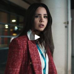 a woman standing next to a building wearing a red blazer and blue striped shirt