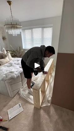 a man standing on top of a wooden block in a bedroom next to a bed