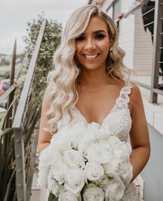 a woman in a wedding dress holding a bouquet of flowers and smiling at the camera