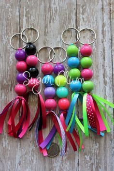 several key chains with different colored beads and ribbons hanging from them on a wooden surface