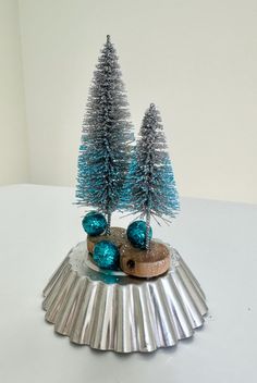 two small christmas trees sitting on top of a tinsel covered cake pan with blue decorations