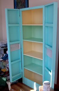 an open bookcase in the corner of a room with other items on the floor