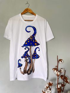 Discover the charm of nature with our exclusive hand-painted mushroom t-shirt. Each piece is meticulously hand-painted, ensuring 100% uniqueness. The minimalist design effortlessly complements any outfit in your wardrobe. ✨Customize the color scheme to suit your style. ✨Modify the shape and number of mushrooms to create your perfect look. ✨The color combinations for the mushrooms are limitless, allowing for a truly personalized touch. The drawing is applied by hand with brushes and special paints. Therefore, each product is not 100% similar to the previous one and is unique. Made from high-quality cotton material, our mushroom t-shirt offers unbeatable comfort and breathability, ensuring you feel great all day long. Whether you're out on the town or lounging at home, this t-shirt is the pe Hand Painted White Short Sleeve Tops, White Hand Painted Short Sleeve Tops, Summer Graphic Tee With Mushroom Print, Hand Painted Short Sleeve Cotton Top, Hand Painted Cotton Short Sleeve Top, White Hand Painted Short Sleeve T-shirt, Graphic Tee With Mushroom Design, Artistic Hand Painted Short Sleeve T-shirt, Hand Painted White T-shirt For Summer