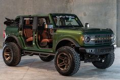 a green jeep with brown leather seats parked in front of a concrete wall and cement floor