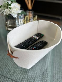 two remote controls in a paper cup on a table next to vases with flowers