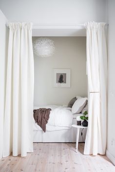 a white bed sitting in a bedroom next to a window with drapes on it