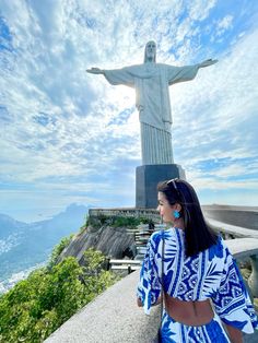 a woman standing in front of the statue of christ on top of a hill looking at the ocean