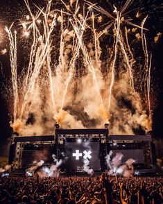 fireworks are lit up in the sky above an outdoor concert stage with large screen screens