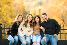 three adults and one child sitting on a bench in front of a fence with fall foliage