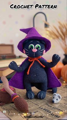 a crocheted black cat wearing a purple witches hat and holding a broom on top of a table