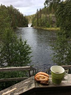 a cup of coffee and some pretzels on a wooden bench by the water