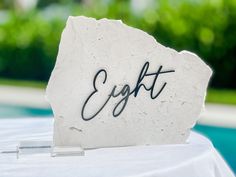 a white rock with the word eight written on it sitting in front of a pool