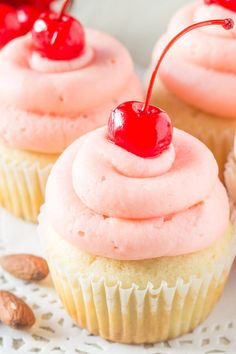 cupcakes with pink frosting and cherries are on a white platter