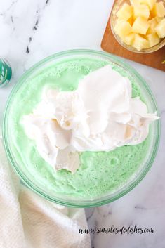 a bowl filled with green pudding next to a wooden cutting board and pineapples