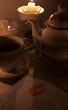 a teapot with a lit candle in it next to two cups and saucers