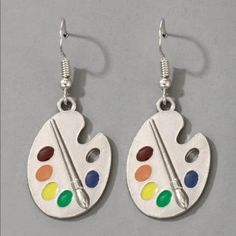 pair of earrings with paintbrush and palettes painted on them, hanging from hooks