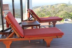 two red lounge chairs sitting on top of a wooden deck next to a glass wall